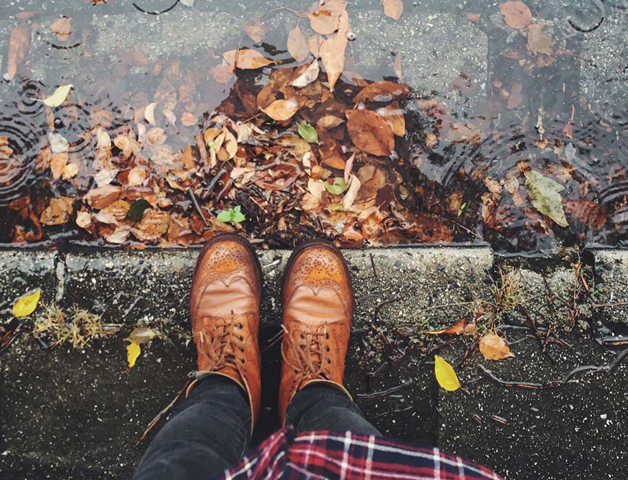 Looking down at shoes and leaves in a puddle.