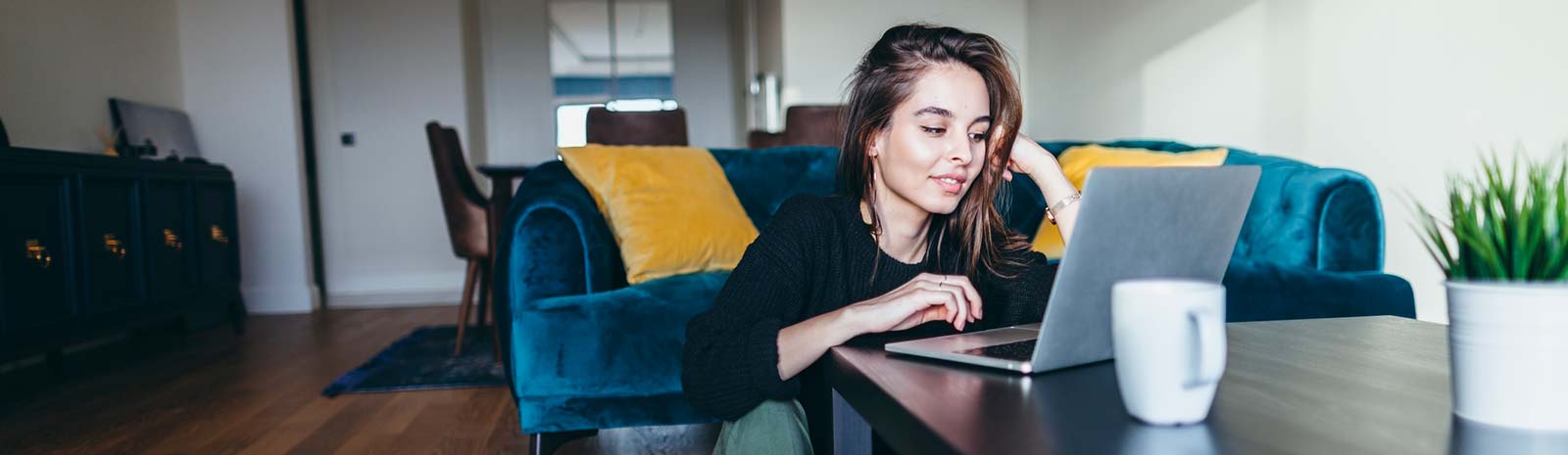 Girl using laptop while seated on floor in living room.