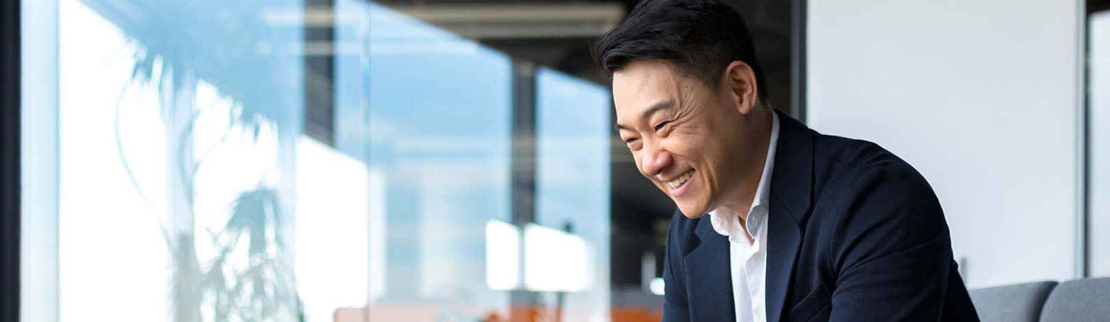 Businessman smiling looking down in glass-walled office.