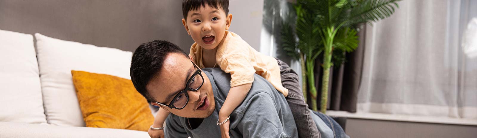 Kid on father's back while doing plank exercise in living room.